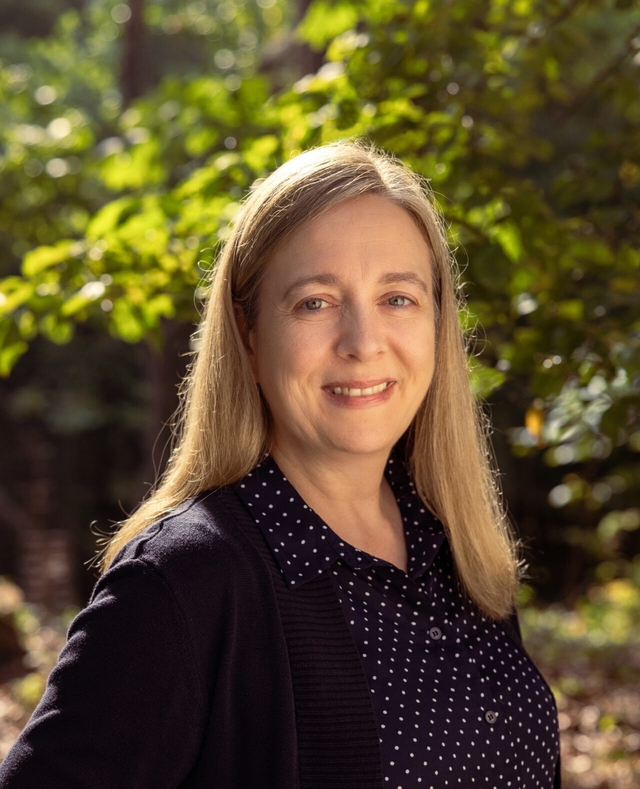 A woman in a dark blue sweater and long hair smiles at the camera