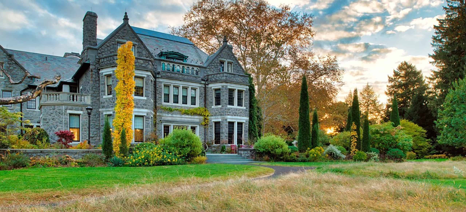 a large stone mansion surrounded by fall foliage and a sunset