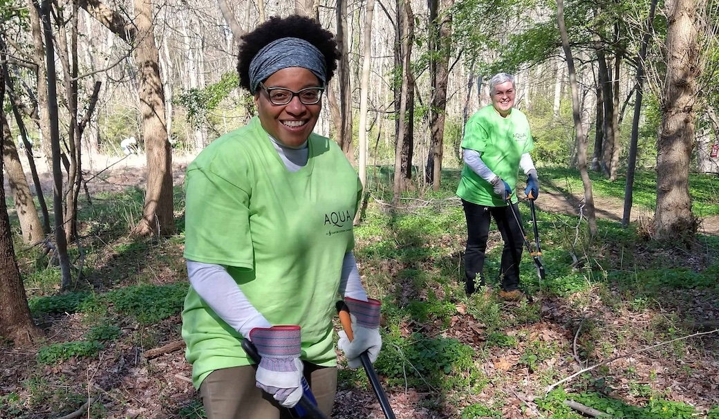Two women with Aqua company shirts on prune invasive vines in a forest.
