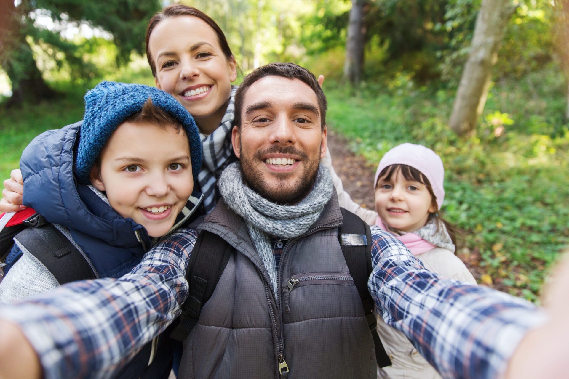 a man, woman, and two children with backpacks smiling and taking a selfie while hiking in the woods